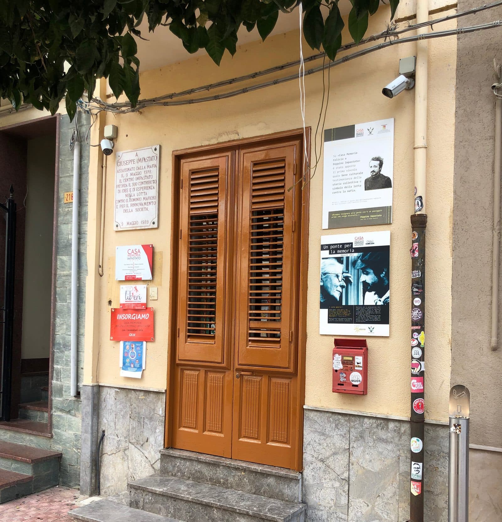 L'ingresso di Casa Memoria Felicia e Peppino Impastato a Cinisi, con la lapide per Peppino e i manifesti alle pareti.